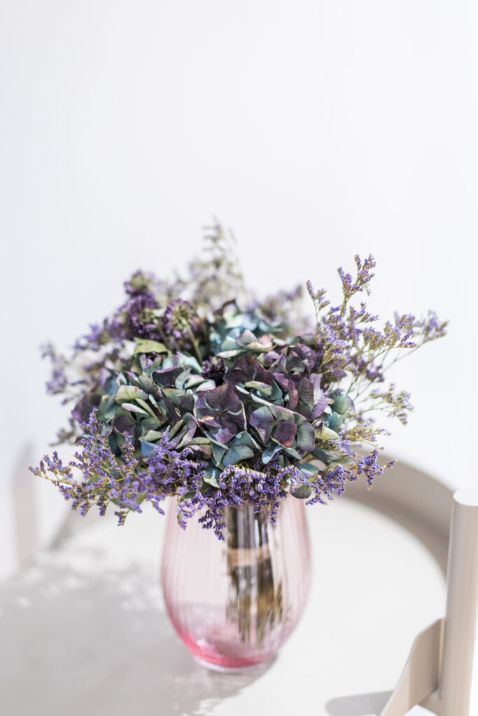 Foto eines kleinen Blumenstraußes in einer rosaroten Glasvase auf einem weißen Beistelltisch